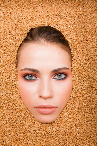 La cara de una hermosa chica de una modelo de moda con maquillaje glamoroso en una dispersión de trigo sarraceno. Concepto de dieta. Disparo de moda —  Fotos de Stock