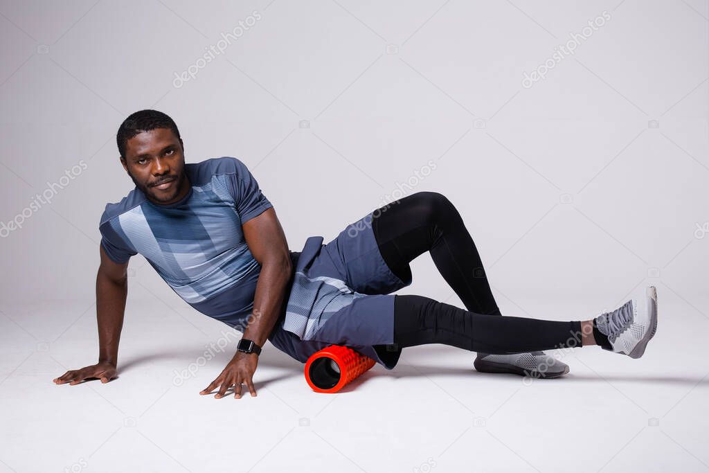 A male pilates trainer in a blue jersey and black tights trains with a red massage roll. Fascia study