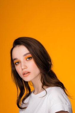 Parlak makyajlı bir kız turuncu bir arka planda duruyor. Sonbahar konsepti