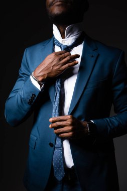 Afrikalı Amerikalı adam yaka ve kravatı elleriyle düzeltiyor.