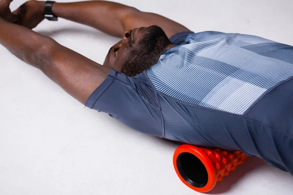 Κοντινό πλάνο. Αρσενικός γυμναστής γυμναστικής γυμνάζει την περιτονία των μυών της πλάτης χρησιμοποιώντας ένα ρολό μασάζ — Φωτογραφία Αρχείου