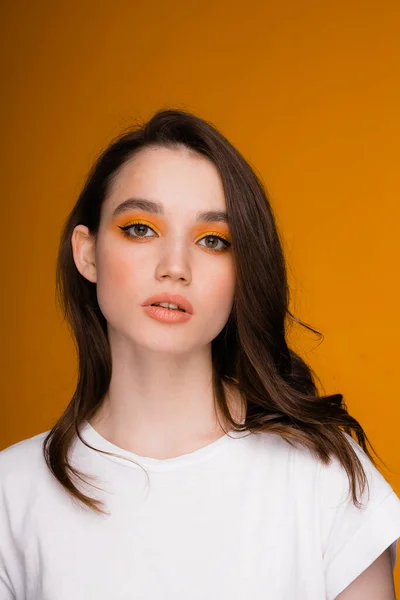 Retrato de una chica de aspecto europeo con maquillaje de ojos brillantes, se levanta sobre un fondo naranja —  Fotos de Stock