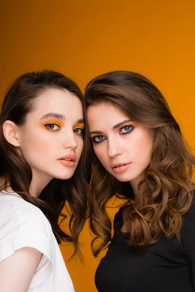 Dos chicas con maquillaje brillante están de pie sobre un fondo naranja. Concepto de otoño. —  Fotos de Stock