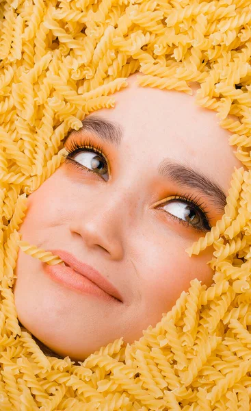 Een schattig meisje met fel oranje make-up ligt in een versnippering van pasta. Concept voor een pandemisch preparaat van het coronavirus — Stockfoto