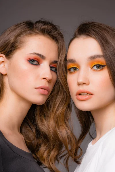 Dos hermosas chicas atractivas con maquillaje rojo brillante y naranja de pie sobre un fondo gris —  Fotos de Stock