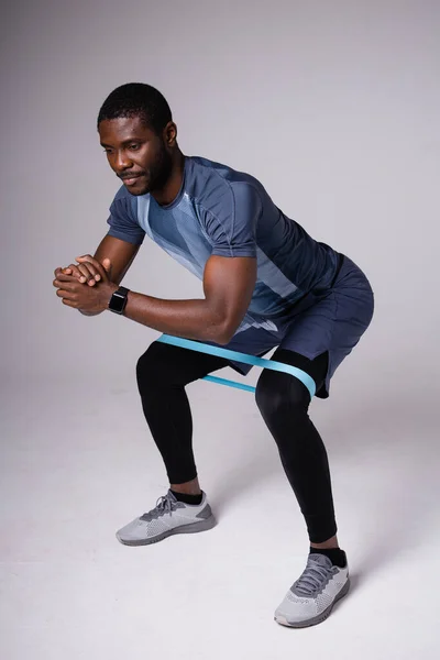 Αφρο-Αμερικανός κάνει καταλήψεις με λάστιχο για προπονήσεις. Γυμναστική σε λευκό φόντο — Φωτογραφία Αρχείου