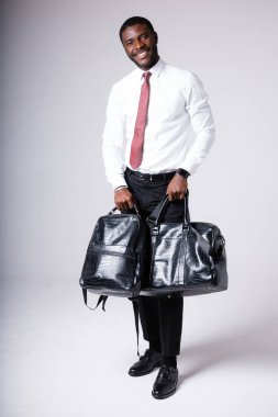Siyah bir sırt çantası ve siyah deri bir çanta tutan esmer bir adam. Beyaz bir arkaplanda durur