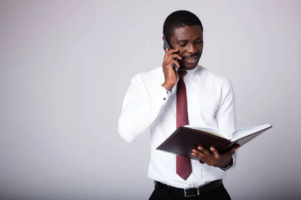 Afroamerykanin w stroju biznesowym trzyma otwartą teczkę z dokumentami i rozmawia przez telefon. Koncepcja zdalnej pracy w kwarantannie — Zdjęcie stockowe