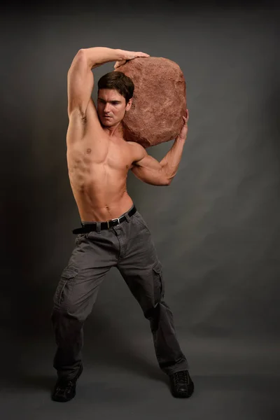 セクシーな男は彼の頭の上に巨大な岩を保持します — ストック写真