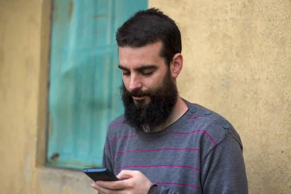 Bearded Young Man Looking Mobile Outdoors Wall Cottage Background — Stock Photo, Image