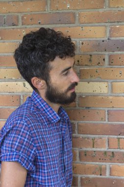 Tuğla duvara yaslanan düşünceli genç adamın profil görüntüsü