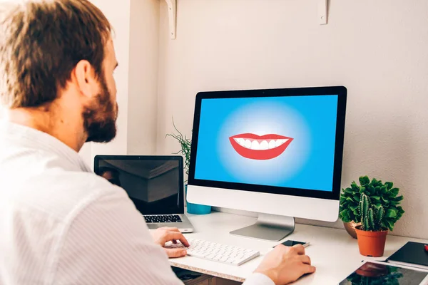 Young man using computer with dental care concept on the screen on a desk with tablet, laptop, smartphone and plants