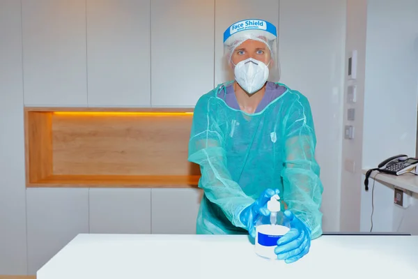 Sağlık çalışanı yüz maskesi takıyor ve klinik resepsiyonunda elleri için hidroseksüel jel sunuyor.