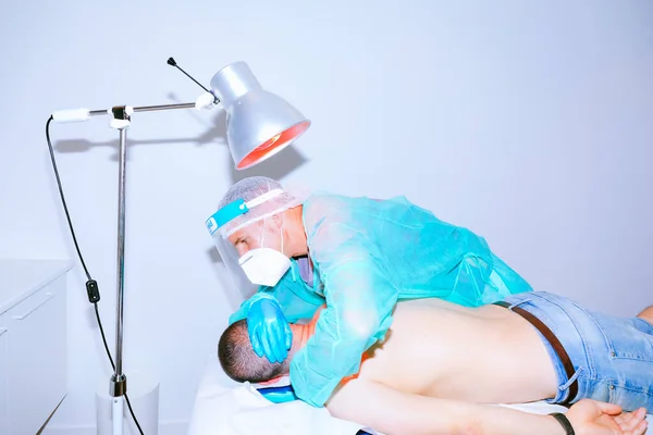 Physiotherapist wearing face shield, mask and latex gloves is stretching patient\'s neck