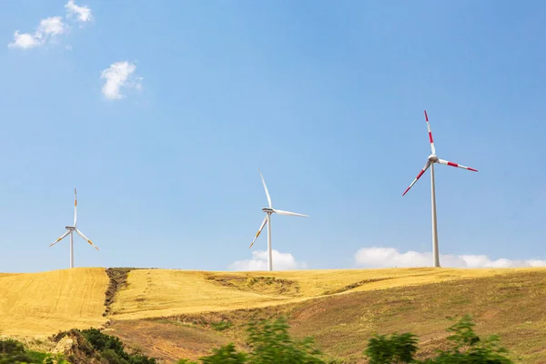 Three wind-driven electric generators against a yellow field and blue sky. Summer sunny day.