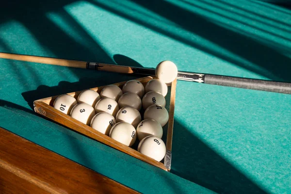 Billiard balls arranged in a triangle rack with cues on table