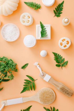 Şeftali rengi arka planda yeşil yapraklı banyo aksesuarları ve doğal kozmetik ürünleri.
