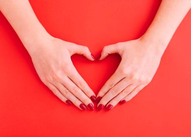 Kadın elleri kırmızı arka planda bir kalp sembolü gösterir. Metin için yer.