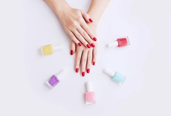 Nail Polish. Art Manicure. Multi-colored Nail Polish Bottles around female hands with stylish red nails