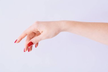 Açık gri arka planda kırmızı manikürlü bir kadın eli.