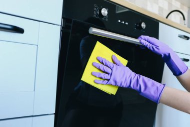 Kadın, koruyucu eldivenleriyle fırını bez parçasıyla temizliyor.