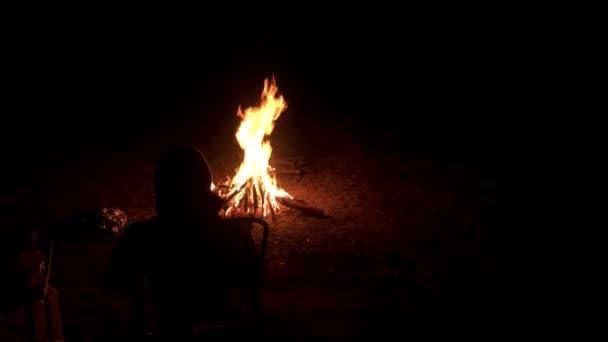 Un homme est assis dans un fauteuil près du feu lumineux sur une côte nocturne — Video