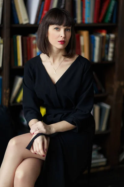 Брюнетка в черном платье на фоне книг — стоковое фото