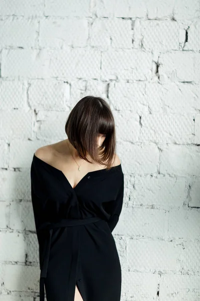 Foto de jovem morena em vestido preto contra parede de tijolo branco — Fotografia de Stock