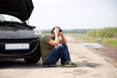 Açık hood ile kırık araba yanında oturan sinirli adam görüntüsünü