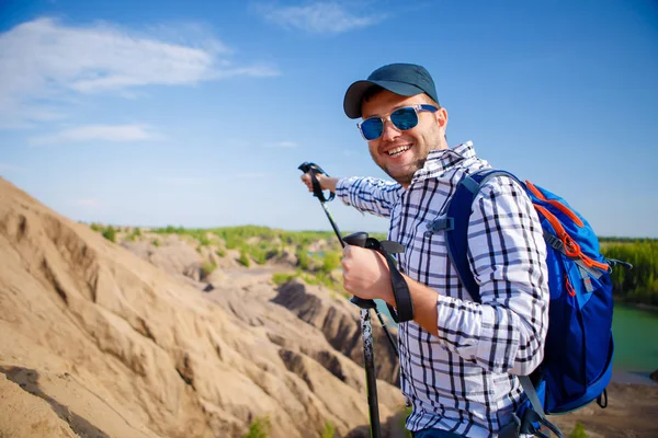 Foto des fröhlichen Touristenmannes mit Rucksack, der sich mit Stöcken nach vorne streckt, um auf dem Hügel zu gehen — Stockfoto