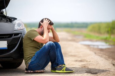 Hayal kırıklığına uğramış adamın yanında kırık araba ile açık örtünün oturan resmi