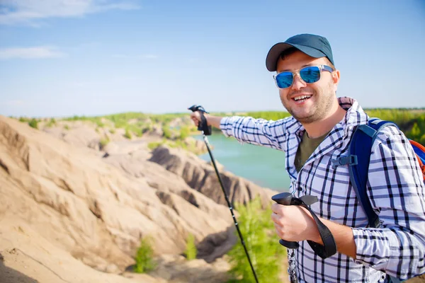 Bild eines fröhlichen Touristenmannes mit Rucksack, der sich mit Stöcken nach vorne streckt, um auf einem Hügel zu gehen — Stockfoto