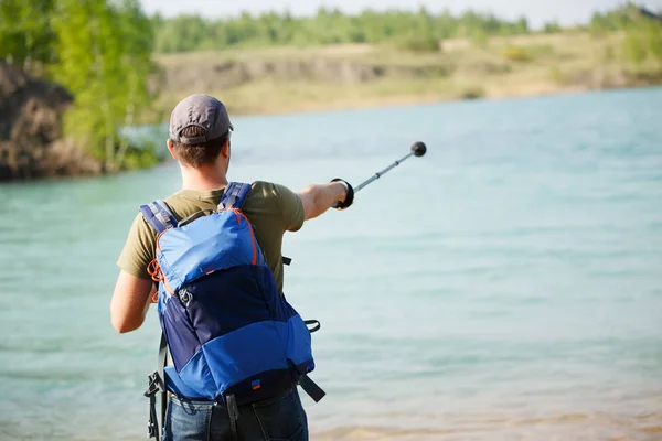 Foto de volta do turista masculino apontando com pau para caminhar para a frente contra o pano de fundo do lago e arbustos verdes — Fotografia de Stock