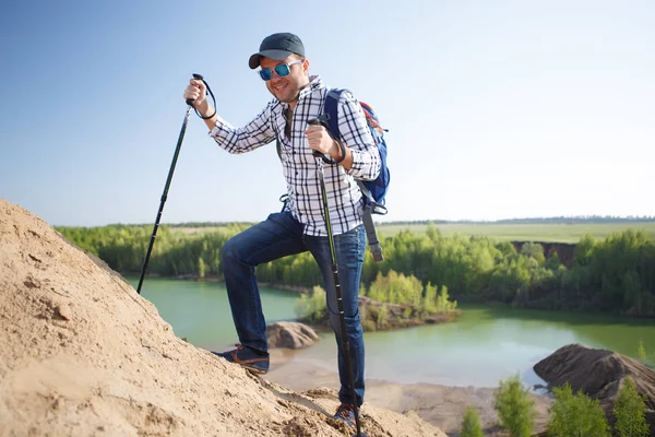 Photo of tourist man with backpack with sticks for walking on hill — Stock Photo, Image
