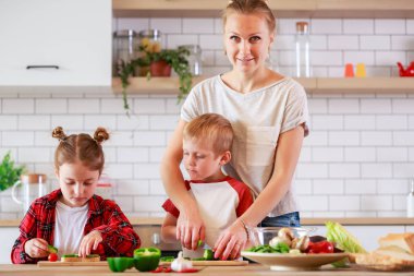 Görüntü bir anne ile kızı ve oğlu masada yemek