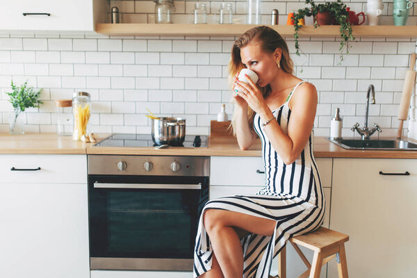 Photo of beautiful woman in long striped dress in kitchen