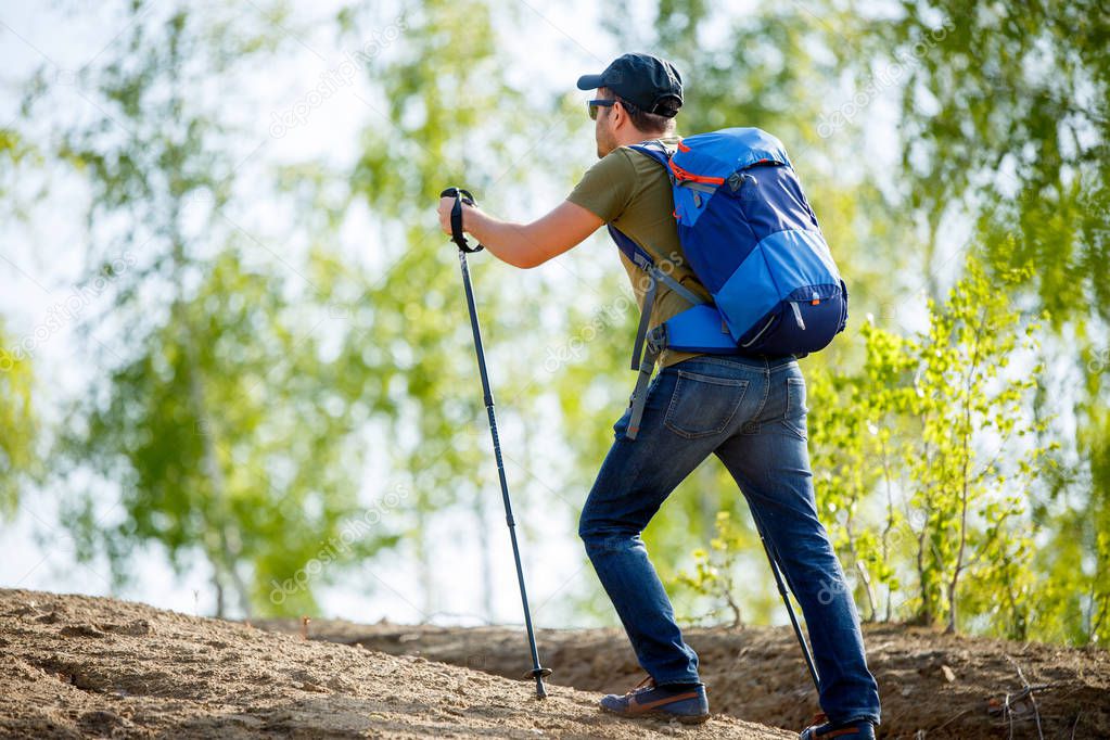 Image from back of man with backpack and walking sticks on hill