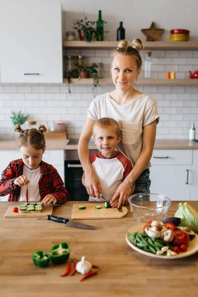 Foto mladé matky s dcerou a synem krájení zeleniny u stolu — Stock fotografie