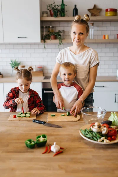 Foto mladé matky s dcerou a synem krájení zeleniny u stolu — Stock fotografie