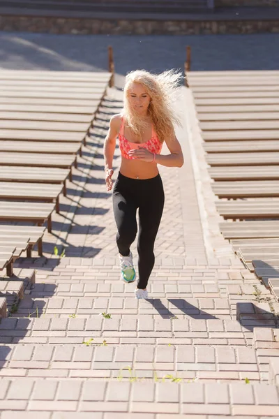 Fotó göndör hajú sportos nő fut keresztül, park padok között — Stock Fotó