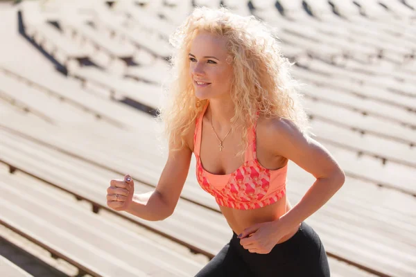 Photo of curly-haired athletic woman running through park among benches — Stock Photo, Image