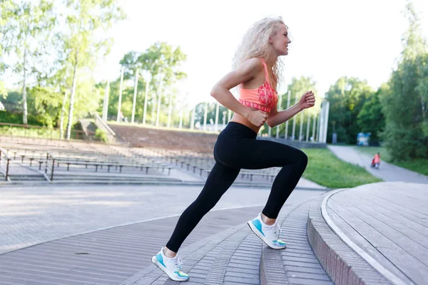 Fotó göndör hajú sportos nő fut keresztül, park padok között — Stock Fotó
