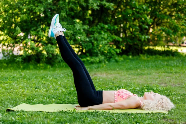 Immagine di giovane donna sportiva dai capelli ricci che pratica yoga sul tappeto nel parco — Foto Stock
