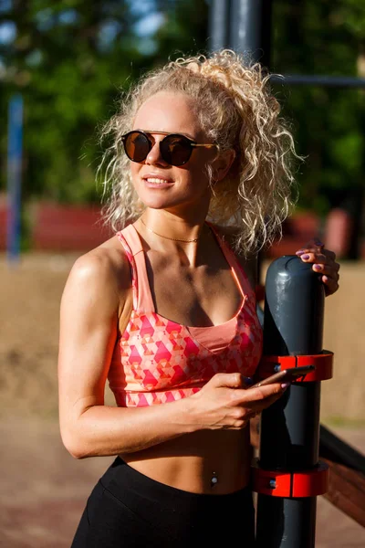 Foto av sport kvinna bär solglasögon håller telefonen i händerna på park — Stockfoto