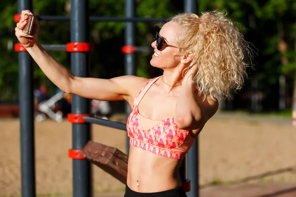 Foto van lachende sport vrouw dragen van een zonnebril doet selfie in park — Stockfoto