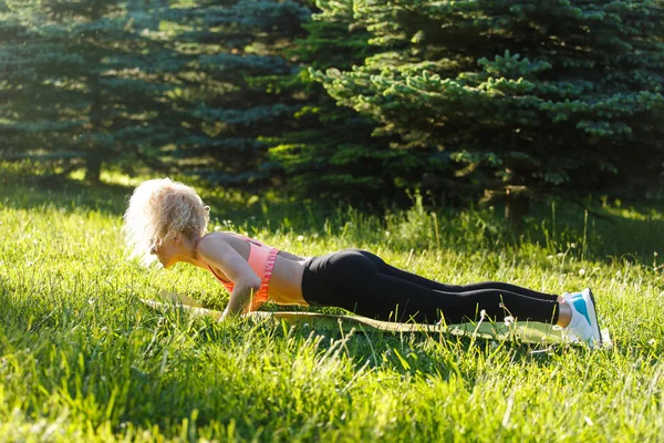 Foto van jonge curly-haired sport vrouw beoefenen van yoga op tapijt in park — Stockfoto