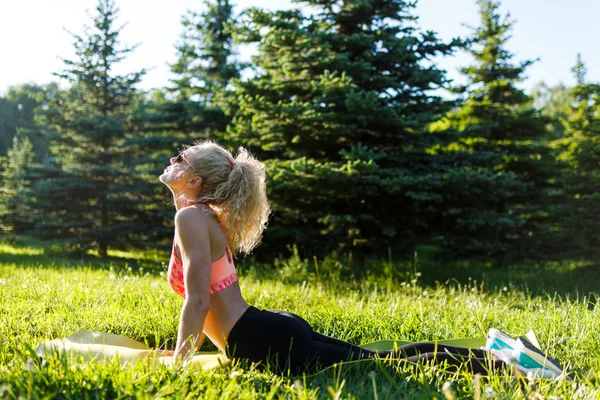 Foto van jonge curly-haired sport vrouw beoefenen van yoga op tapijt in park — Stockfoto