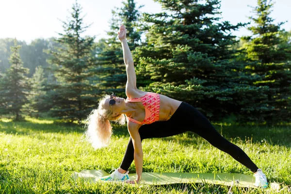 Foto della giovane donna sportiva dai capelli ricci che pratica yoga sul tappeto nel parco — Foto Stock