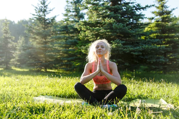 Foto av unga curly-haired sport kvinna utövar yoga på matta i park — Stockfoto