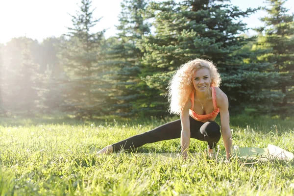 Beeld van jonge curly-haired sport vrouw beoefenen van yoga op tapijt in park — Stockfoto